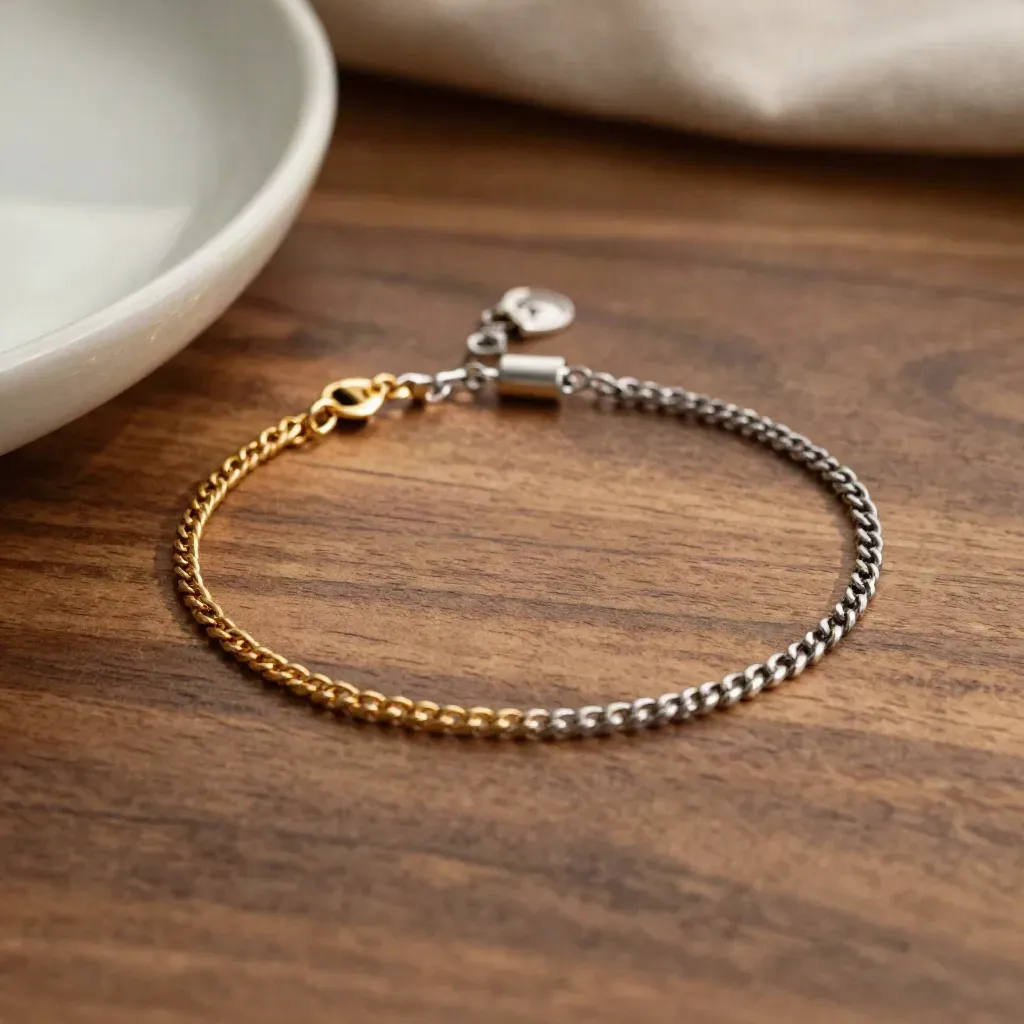 Pulseras de cadena sobre madera cálida y cerámica clara con luz suave arriba.